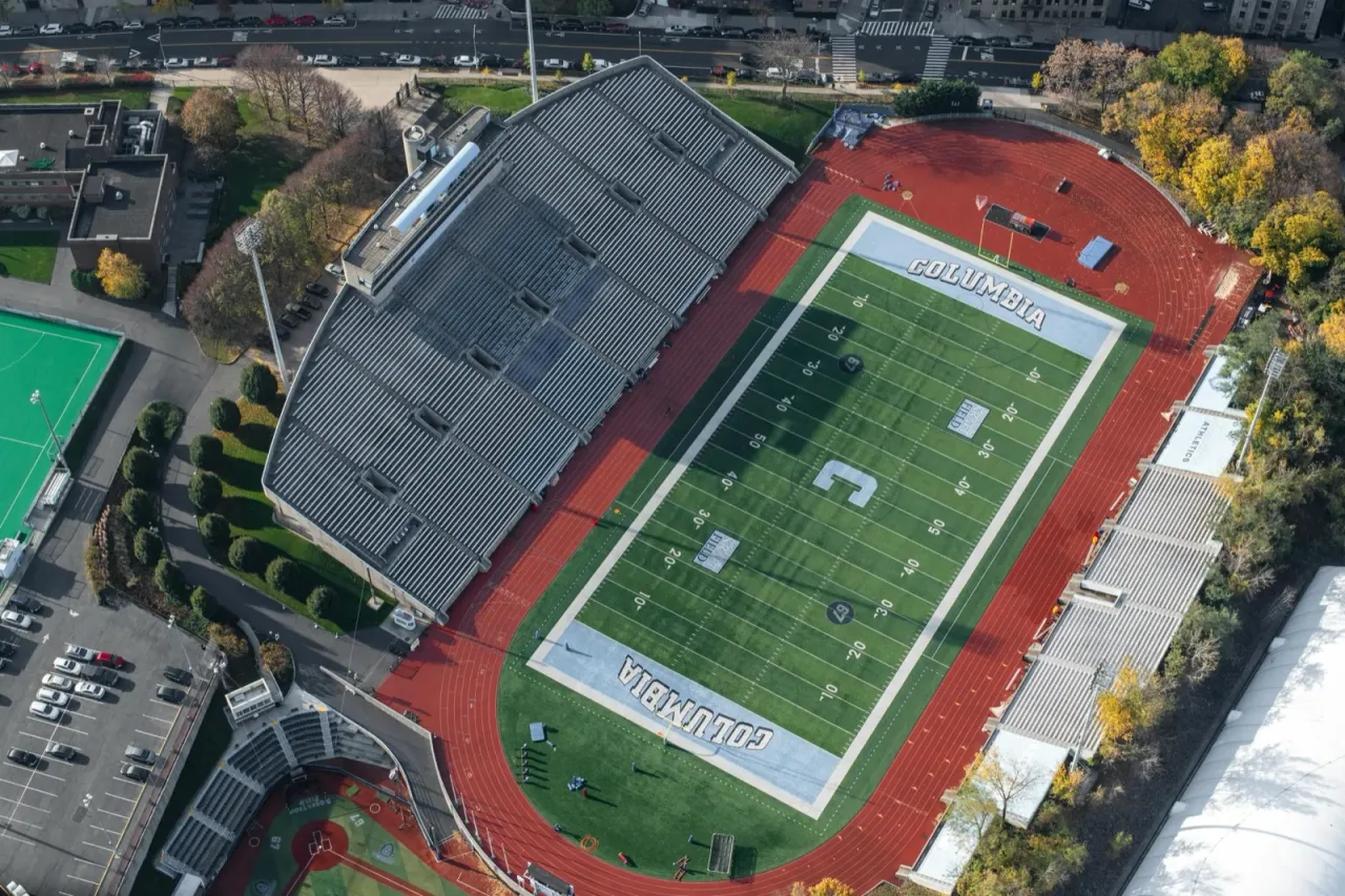 Aerial view of a college athletics stadium showing the red running track surrounding a football field