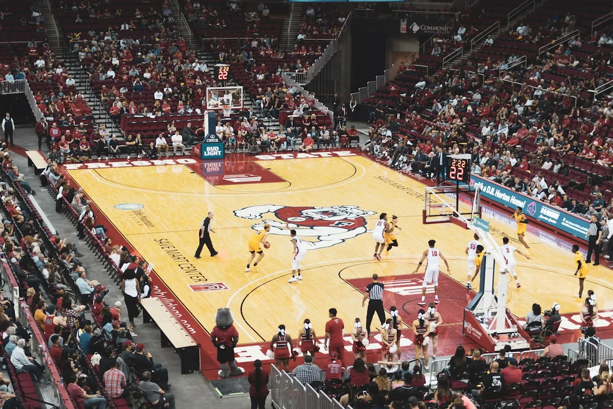 A college basketball player shooting a jump shot during a game in a college arena