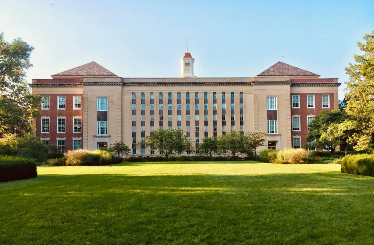 A brick academic hall with a cupola and green hedges on a college campus