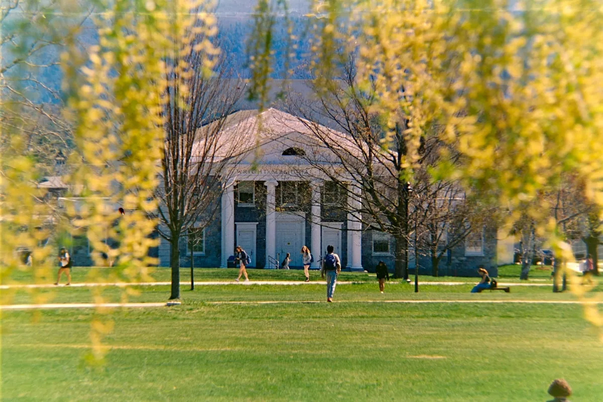 A columned academic hall in spring with students sitting on the lawn