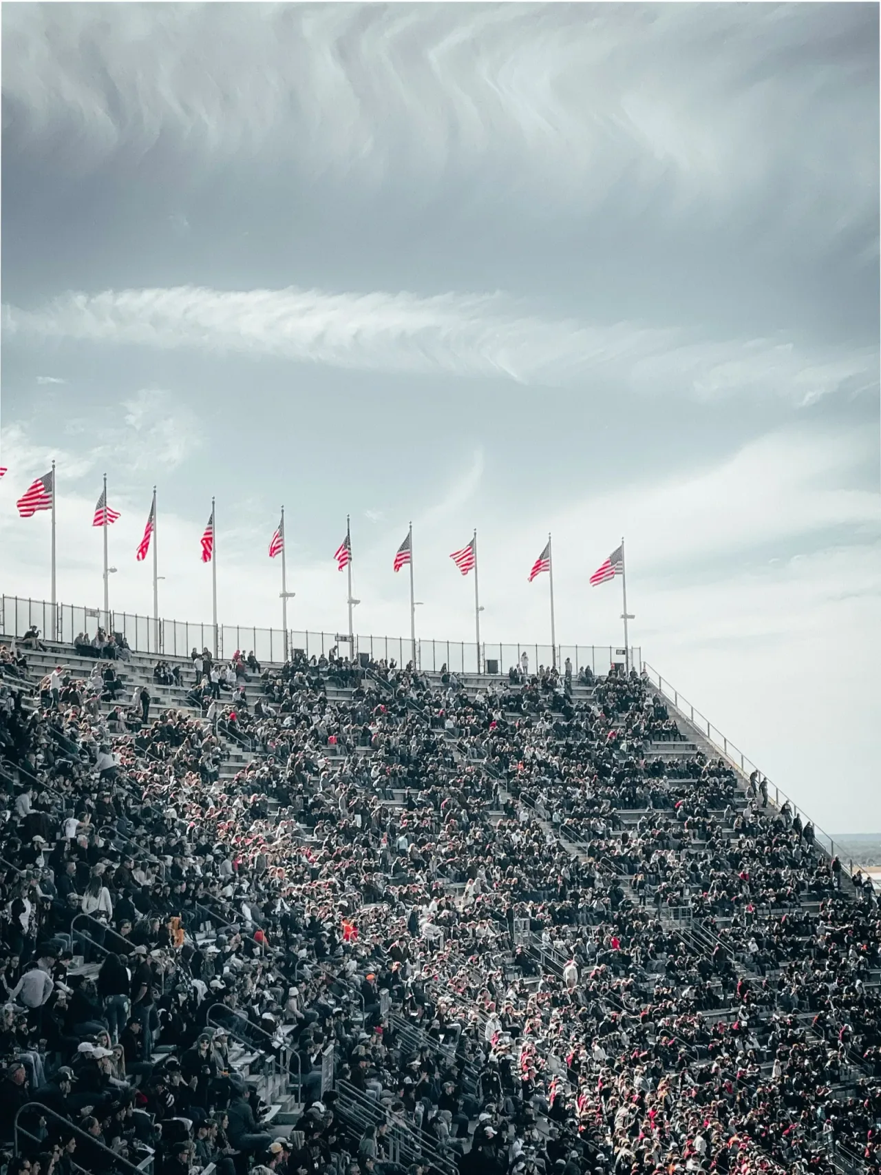 Crowded stadium bleachers with American flags waving against the sky