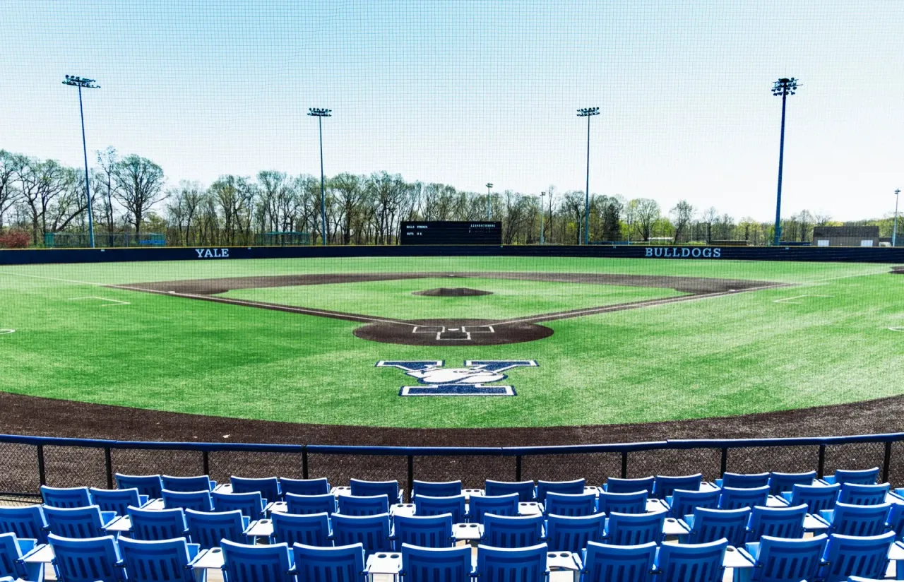 A college baseball stadium with green outfield grass and stadium seating visible