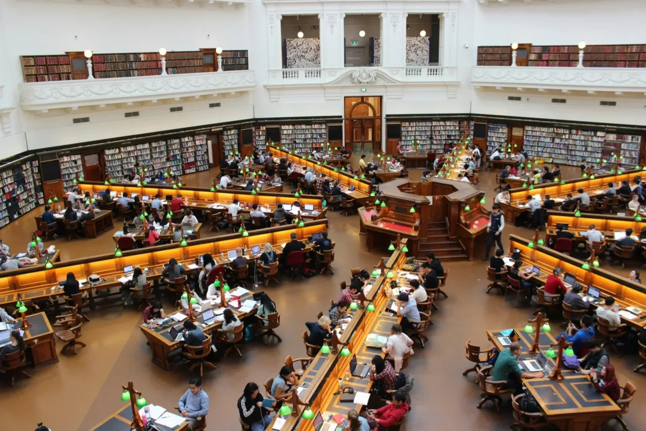 A grand library reading room with students studying at long wooden tables