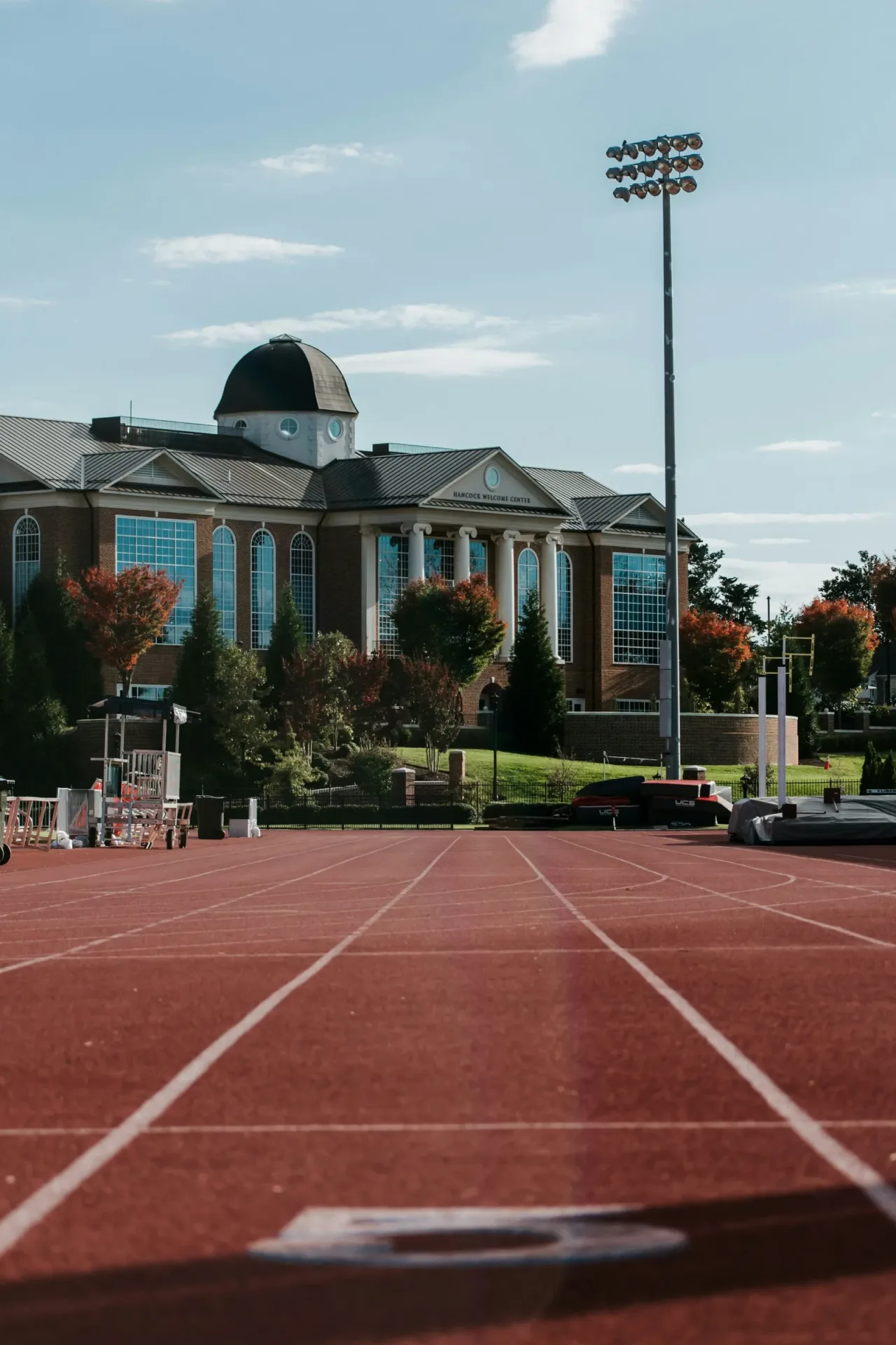 Red running track in front of a college campus building at dusk