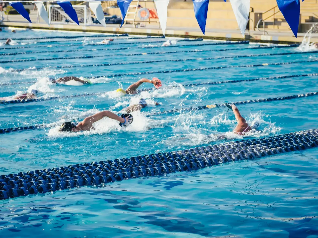 Swimmers racing freestyle in an outdoor pool with multiple lane dividers