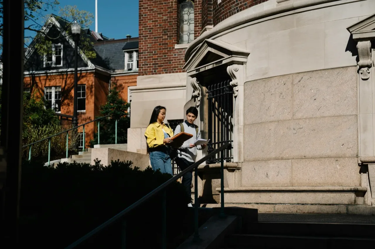 Two college students sitting on campus steps reading together