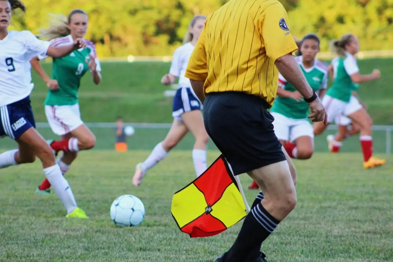Women's soccer match with players running and a linesman holding a flag near the touchline